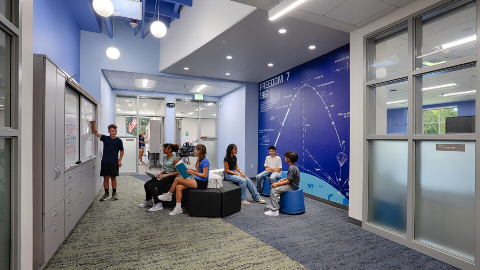 Students collaborating in a modern school hallway with whiteboard cabinets and a blue Freedom 7 wall mural.