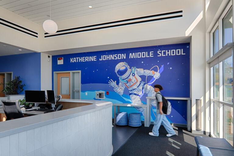 School lobby with reception desk, student walking by, and a mural reading Katherine Johnson Middle School with an astronaut