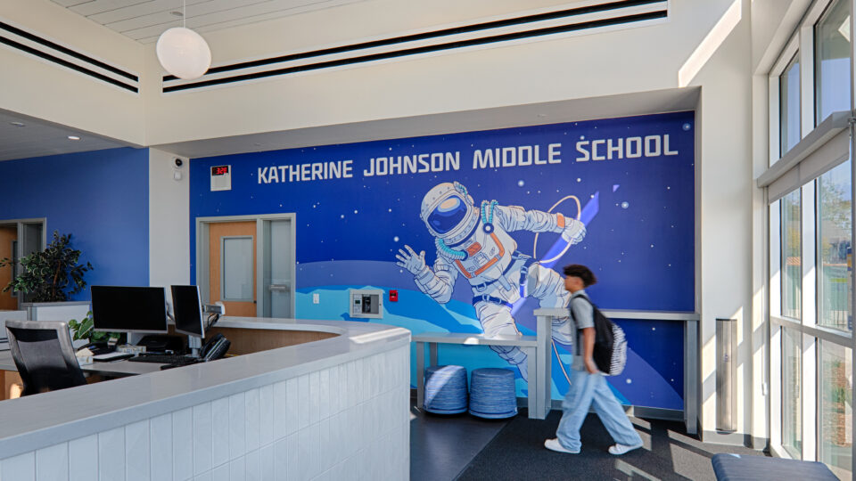 School lobby with reception desk, student walking by, and a mural reading Katherine Johnson Middle School with an astronaut