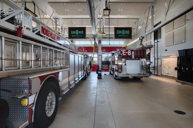 Interior of a Roseville fire station with ladder and engine trucks parked in bright apparatus bays.