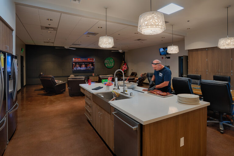 Fire station lounge and kitchen with a firefighter preparing food, recliners, and a Roseville Fire sign on the wall