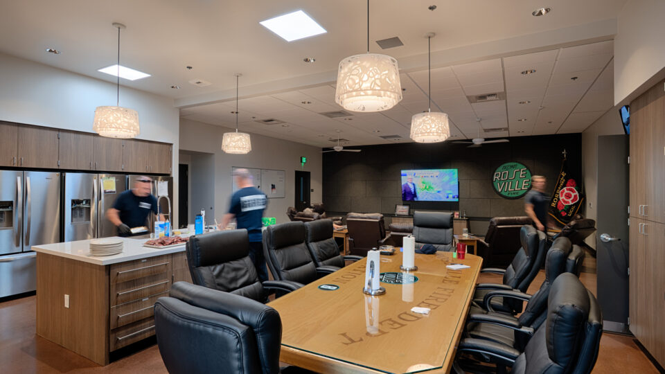 Modern fire station lounge with a long conference table, kitchen island, recliners, and Roseville Fire signage on the wall.