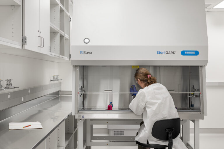 Scientist in a white lab coat working at a SterilGARD biosafety cabinet in a bright laboratory.