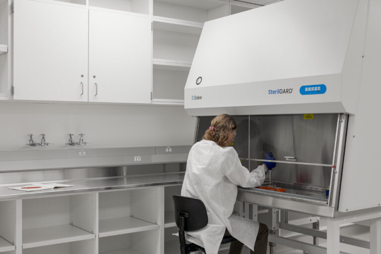 Scientist in a white lab coat working inside a SterilGARD biosafety cabinet in a clean laboratory.