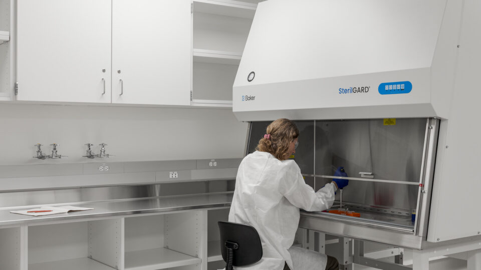 Scientist in a white lab coat working inside a SterilGARD biosafety cabinet in a clean laboratory.