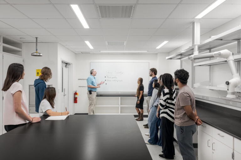 Instructor giving a lab safety briefing to a group of students in a bright science classroom.