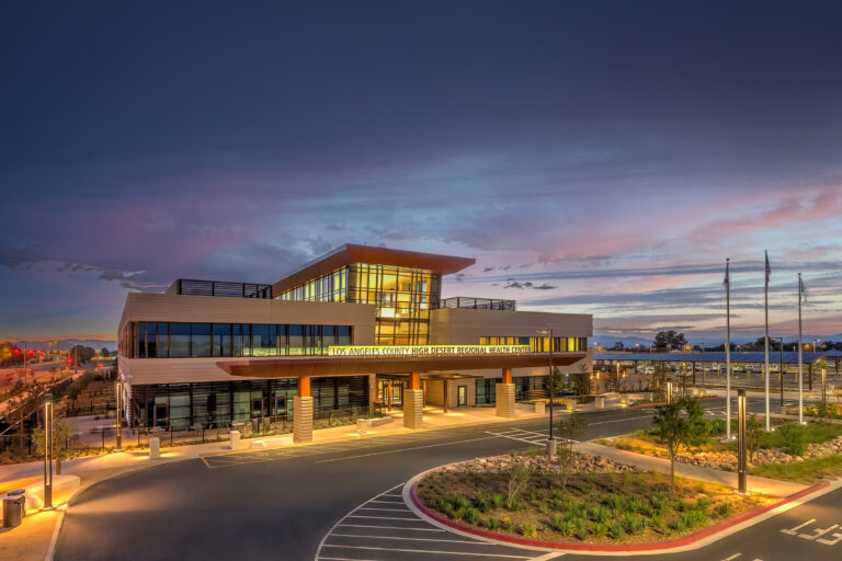 Los Angeles County High Desert Regional Health Center at dusk, with lit windows, parking lot, and colorful sky