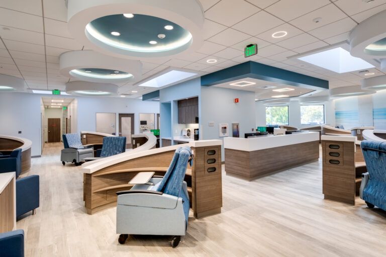 Modern hospital infusion center with curved nursing stations, blue recliners, and bright circular ceiling lights