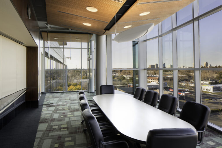 Modern conference room with a long white table, black chairs, floor-to-ceiling windows, and city views.