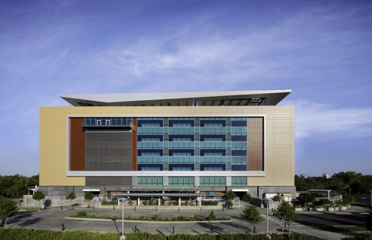 Modern multi-story office building with a glass facade and large overhanging roof under a bright blue sky