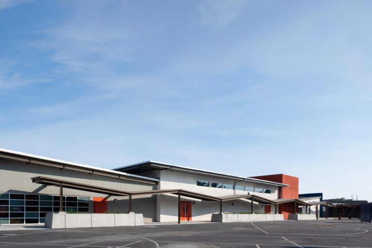 Modern school building with covered walkways and an empty paved courtyard under a blue sky
