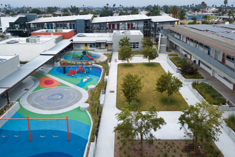 Aerial view of a modern school courtyard with colorful playgrounds, walkways, trees, and surrounding classroom buildings