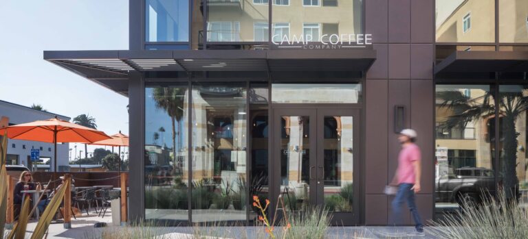 Exterior of Camp Coffee Company with patio umbrellas, glass storefront, and a person walking past.