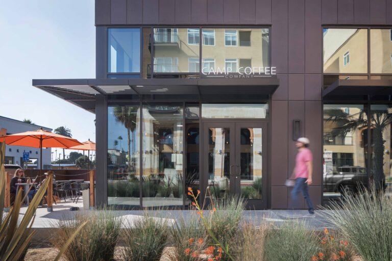 Exterior of Camp Coffee Company with patio umbrellas, glass storefront, and a person walking past.