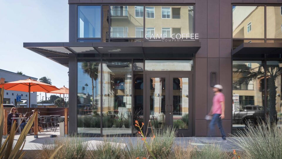 Exterior of Camp Coffee Company with patio umbrellas, glass storefront, and a person walking past.