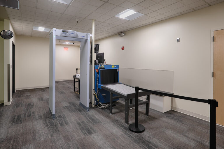 Security screening area with a walk-through metal detector and X-ray conveyor scanner in an office hallway