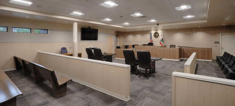 Empty modern courtroom with judge’s bench, witness stand, counsel tables, benches, and U.S. and California flags