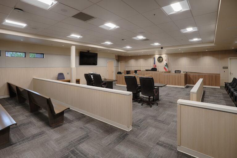 Empty modern courtroom with judge’s bench, witness stand, counsel tables, benches, and U.S. and California flags