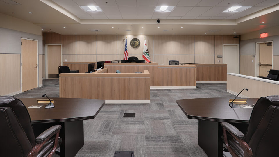 Empty modern courtroom with judge’s bench, witness stand, and U.S. and California flags behind the seal.