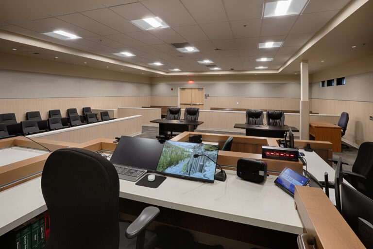 Empty courtroom with judge’s bench, witness stand, jury seating, and clerk’s desk with computer monitors