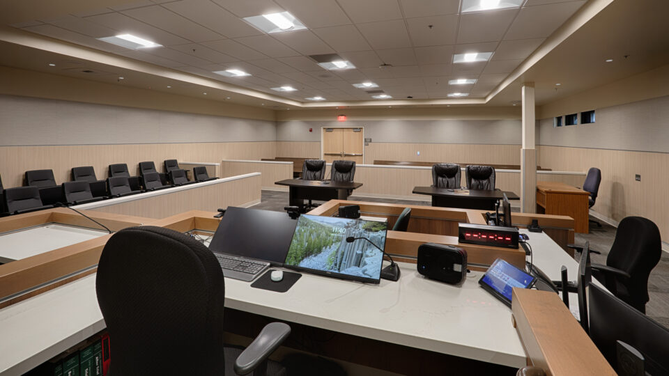 Empty courtroom with judge’s bench, witness stand, jury seating, and clerk’s desk with computer monitors