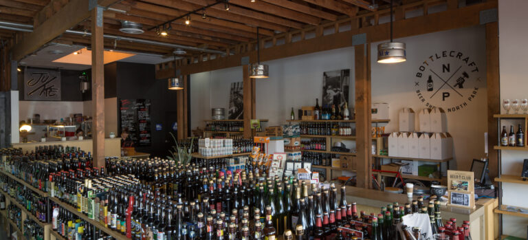 Interior of a craft beer shop with rows of bottled beer and a Bottlecraft North Park sign on the wall.
