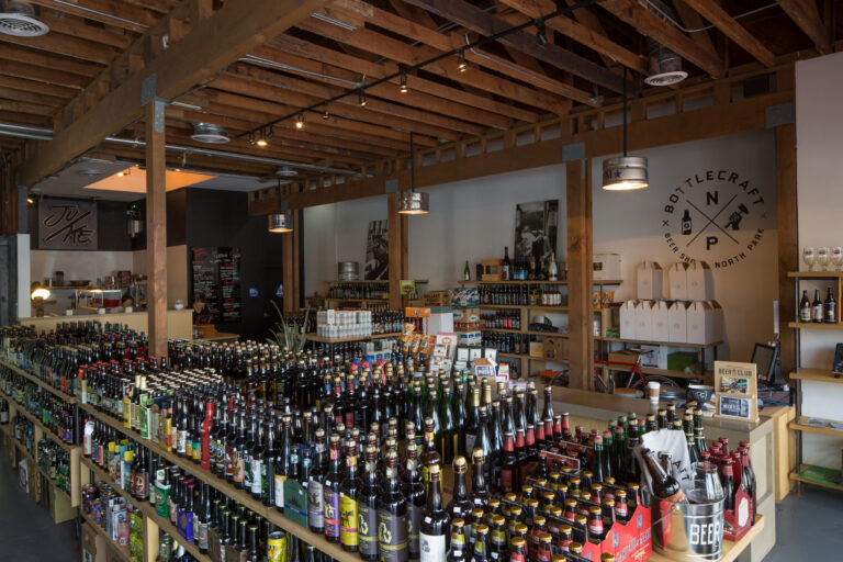 Interior of a craft beer shop with rows of bottled beer and a Bottlecraft North Park sign on the wall.