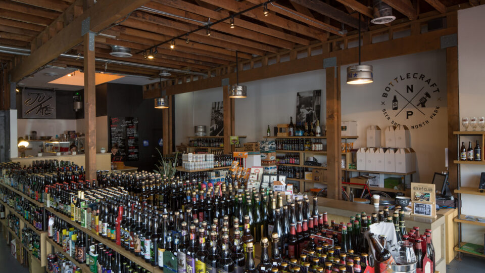 Interior of a craft beer shop with rows of bottled beer and a Bottlecraft North Park sign on the wall.