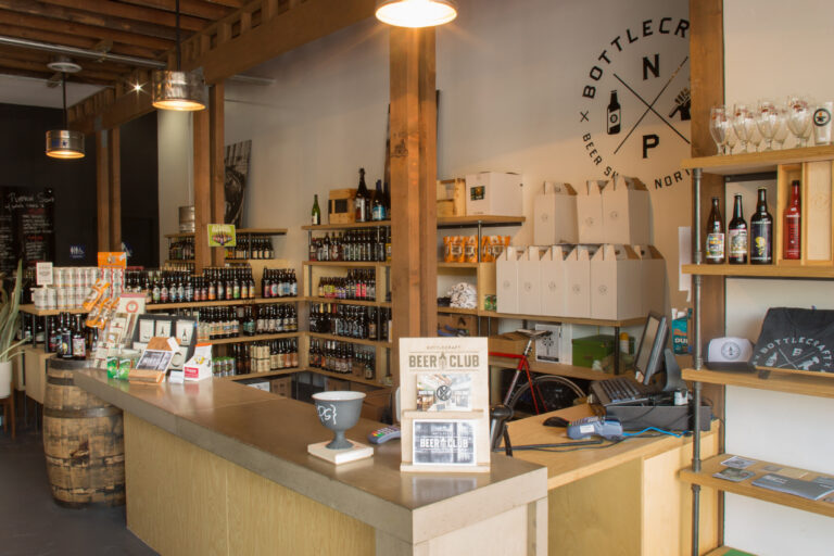 Interior of a craft beer shop with wooden beams, a front counter, and shelves stocked with bottles and glassware