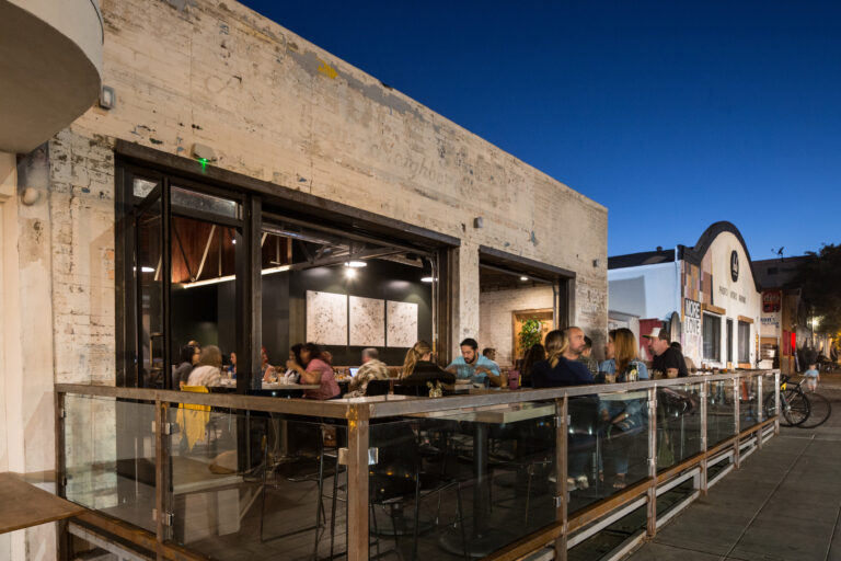 People dining on a restaurant patio outside a weathered building at dusk on a city street
