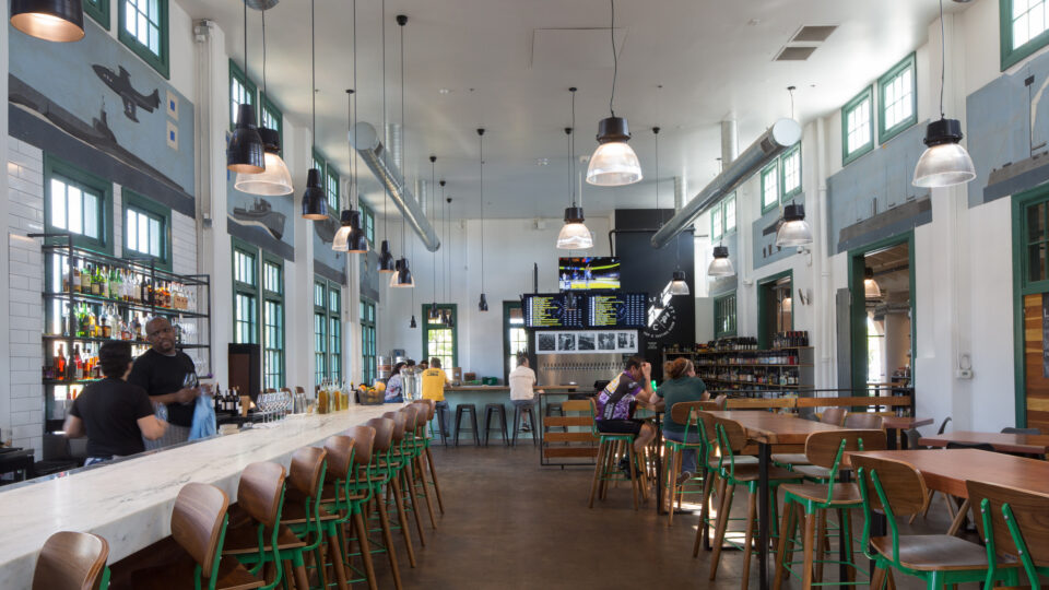 Spacious modern bar and restaurant interior with a long marble counter, green-framed windows, and nautical wall murals