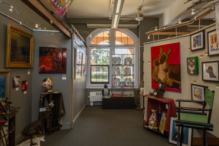 Interior of an art gallery hallway with paintings, animal portraits, sculptures, and a jewelry display by arched windows