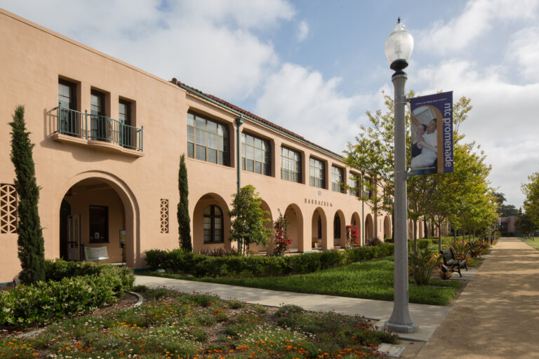 Spanish-style stucco building with arches, landscaped walkway, and an NTC Promenade banner on a lamppost