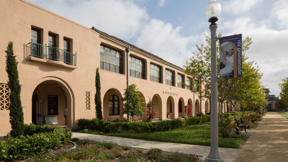 Spanish-style stucco building with arches, landscaped walkway, and an NTC Promenade banner on a lamppost
