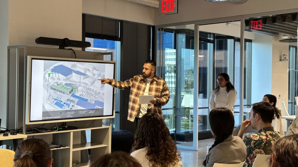 Man points to a water system diagram on a screen while presenting to a small audience in a modern office.