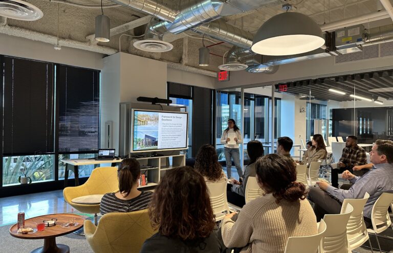 Woman giving a presentation to a seated group in a modern office, with a slide on design and ecosystem impact.