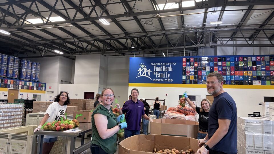 Volunteers sorting produce at Sacramento Food Bank & Family Services warehouse, smiling beside large bins of pears and onions