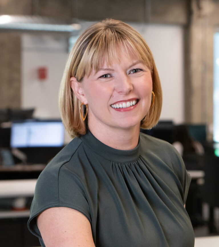 Smiling woman with short blond hair and hoop earrings in a blurred office setting