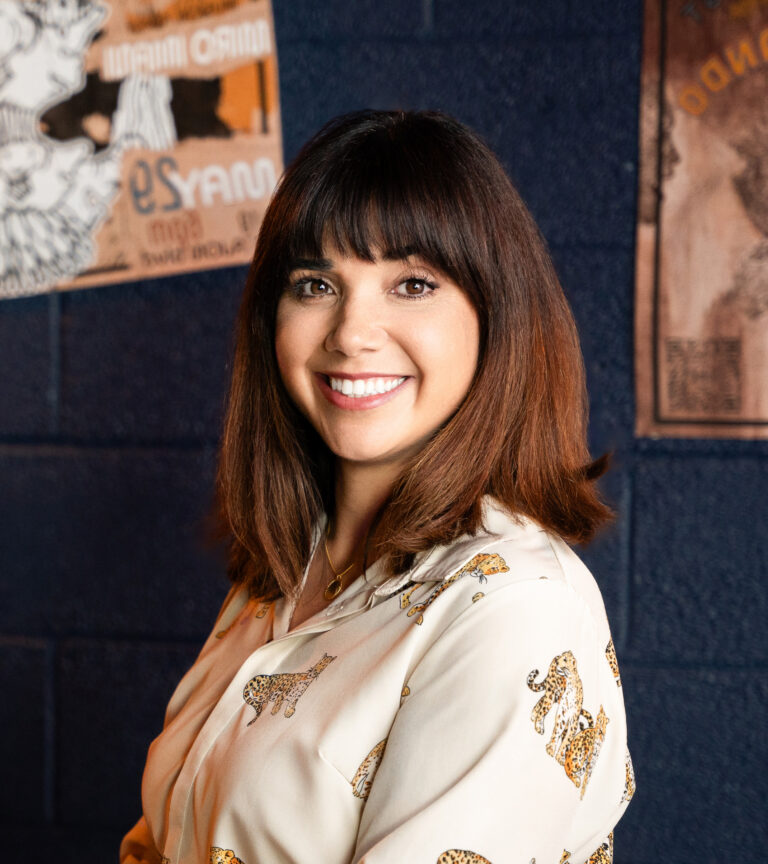 Smiling woman with shoulder-length brown hair and bangs, wearing a cream blouse with leopard print accents.