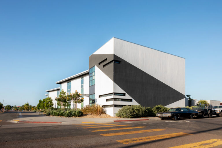Modern white building with a bold black diagonal stripe at a street corner under a clear blue sky