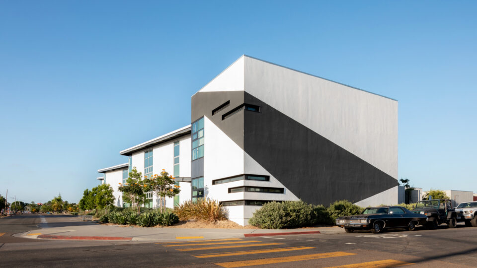 Modern white building with a bold black diagonal stripe at a street corner under a clear blue sky