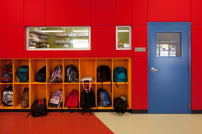 Colorful school hallway with backpacks in yellow cubbies beside a blue door labeled Art Room 108.