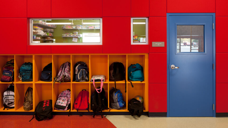 Colorful school hallway with backpacks in yellow cubbies beside a blue door labeled Art Room 108.