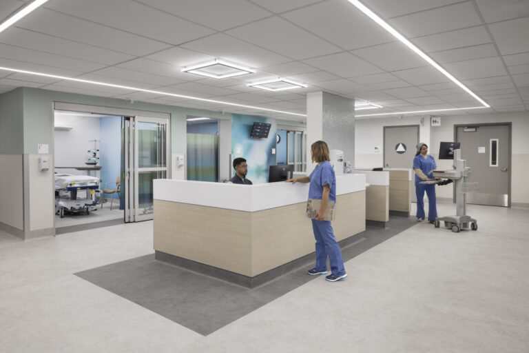 Modern hospital nurse station with staff in blue scrubs, patient rooms, and medical equipment in a bright hallway