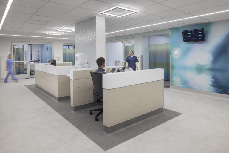 Modern hospital nurses’ station with staff at desks and in hallways, surrounded by patient rooms and soft blue wall graphics