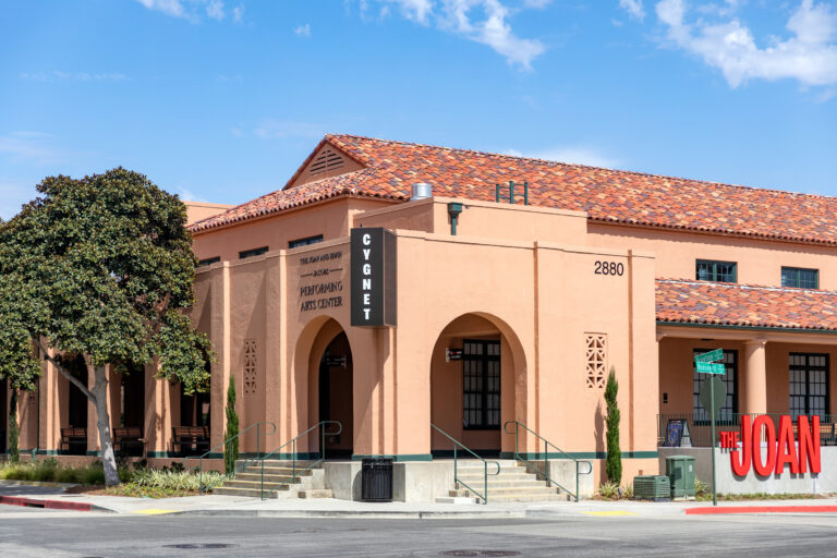The Joan performing arts center building with arched entryways, tile roof, and a Cygnet sign on the corner.