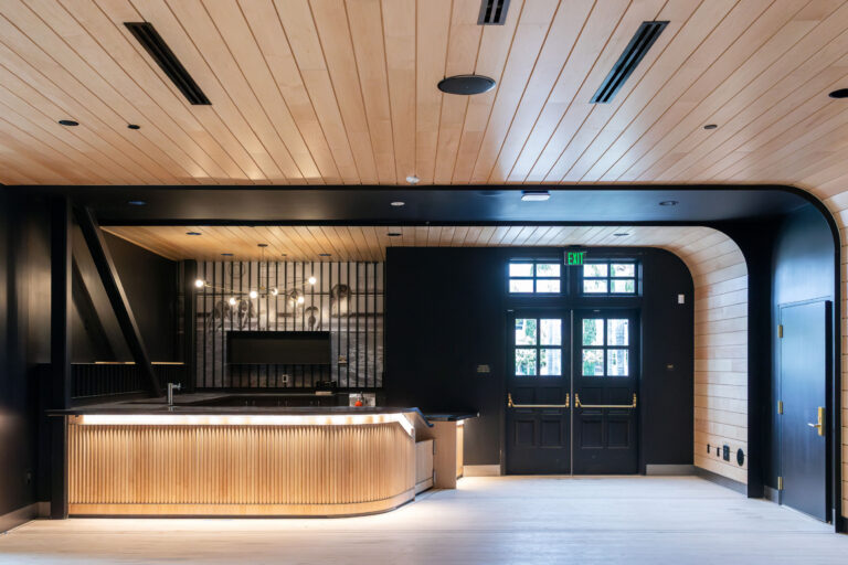 Modern lobby interior with a curved illuminated reception desk, wood-paneled ceiling, and black double exit doors