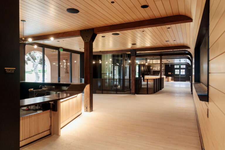 Modern lobby interior with wood ceiling beams, black trim, large windows, and a softly lit reception counter