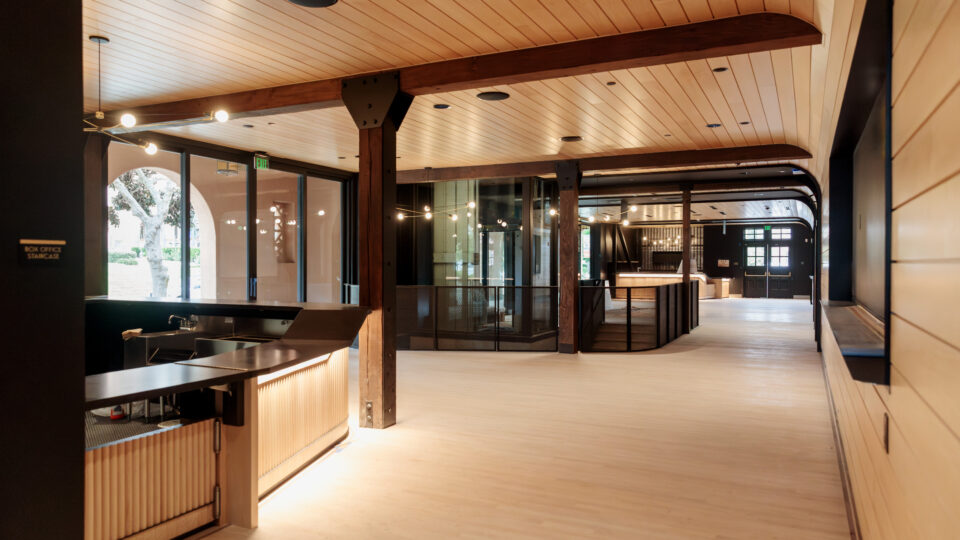 Modern lobby interior with wood ceiling beams, black trim, large windows, and a softly lit reception counter