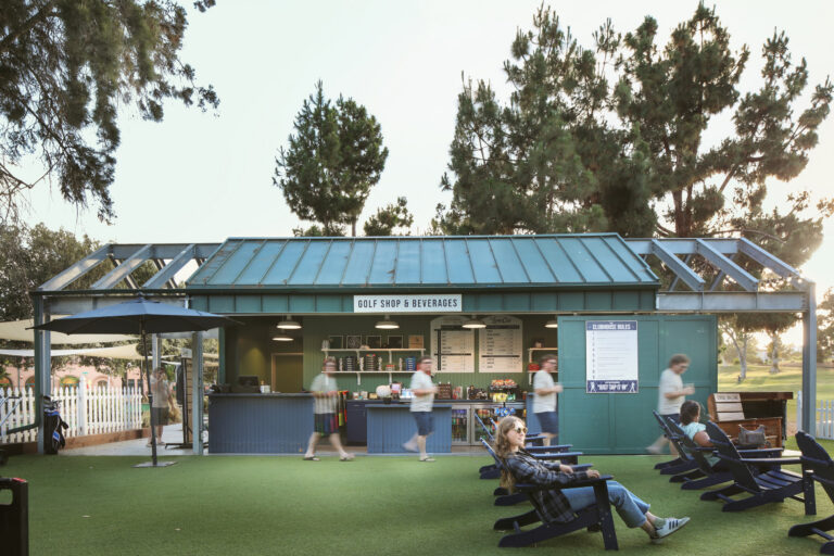 Outdoor golf shop and beverage stand with people walking by and relaxing in chairs on a lawn at sunset